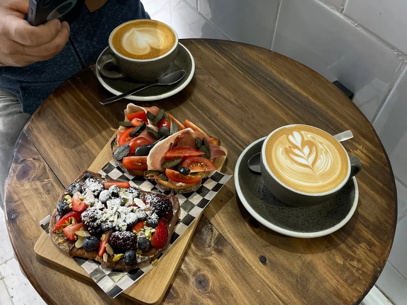 Tostada dulce de berries con cacao y tostada salada con jamón serrano y tomates sobre hogaza artesanal, acompañadas de flat white.