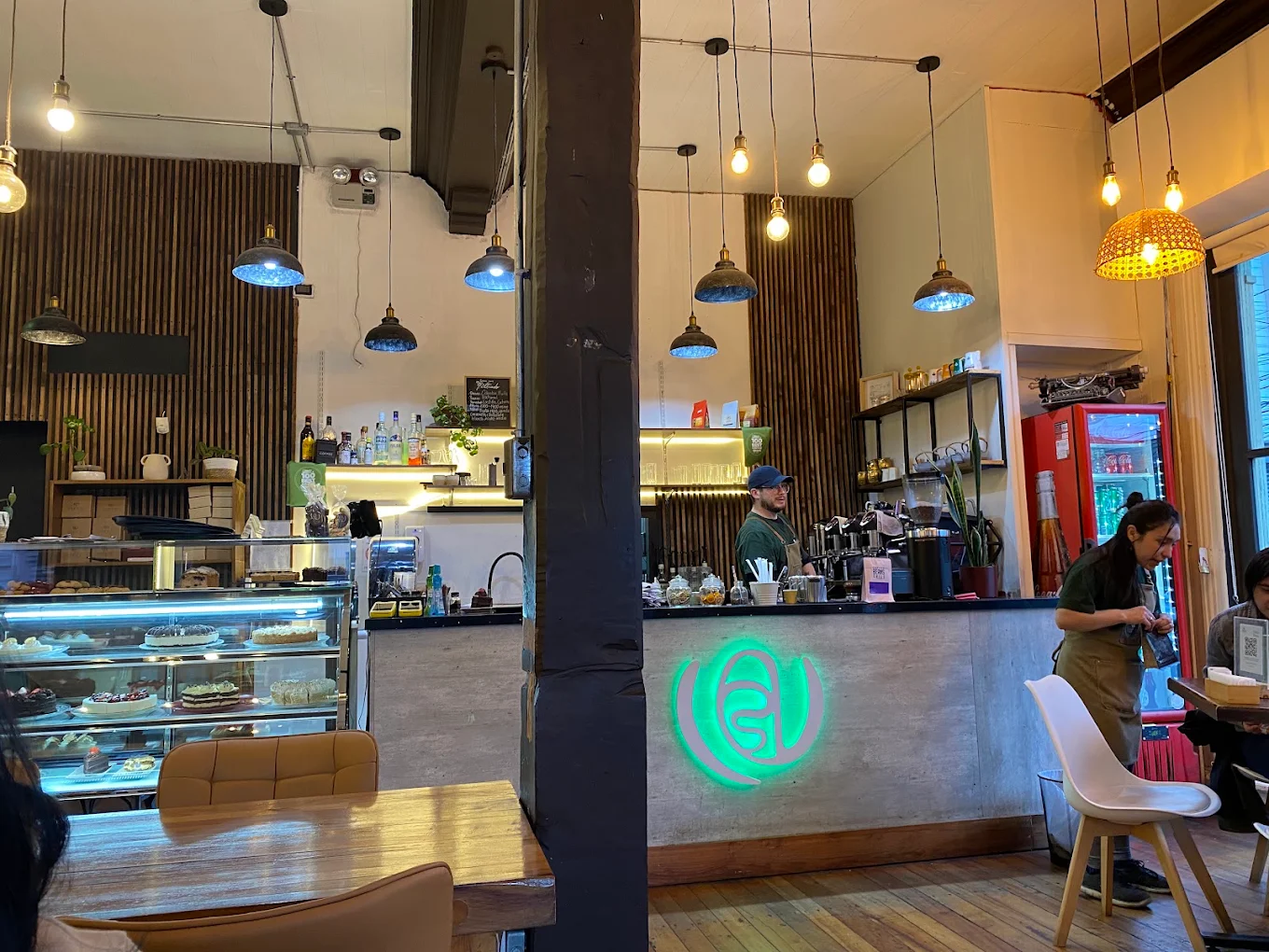 Barra principal de Terra Specialty Coffee con el emblema oficial luminoso en neón verde y vitrina de repostería